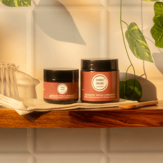Two jars of 'Humble Origins' on a wooden shelf with plants in the background