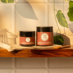 Two jars of 'Humble Origins' on a wooden shelf with plants in the background
