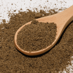 Wooden spoon filled with dark brown powder on a textured surface