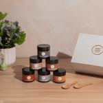 Set of jars with labels on a wooden surface next to a box and flowers.