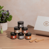 Set of jars with labels on a wooden surface next to a box and flowers.