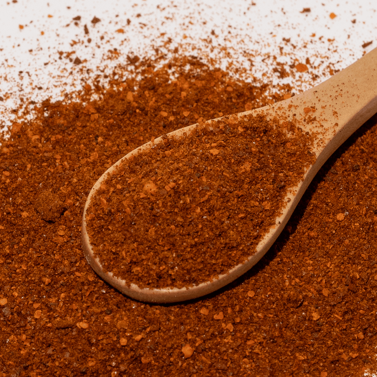 Wooden spoon filled with red chili powder on a white background