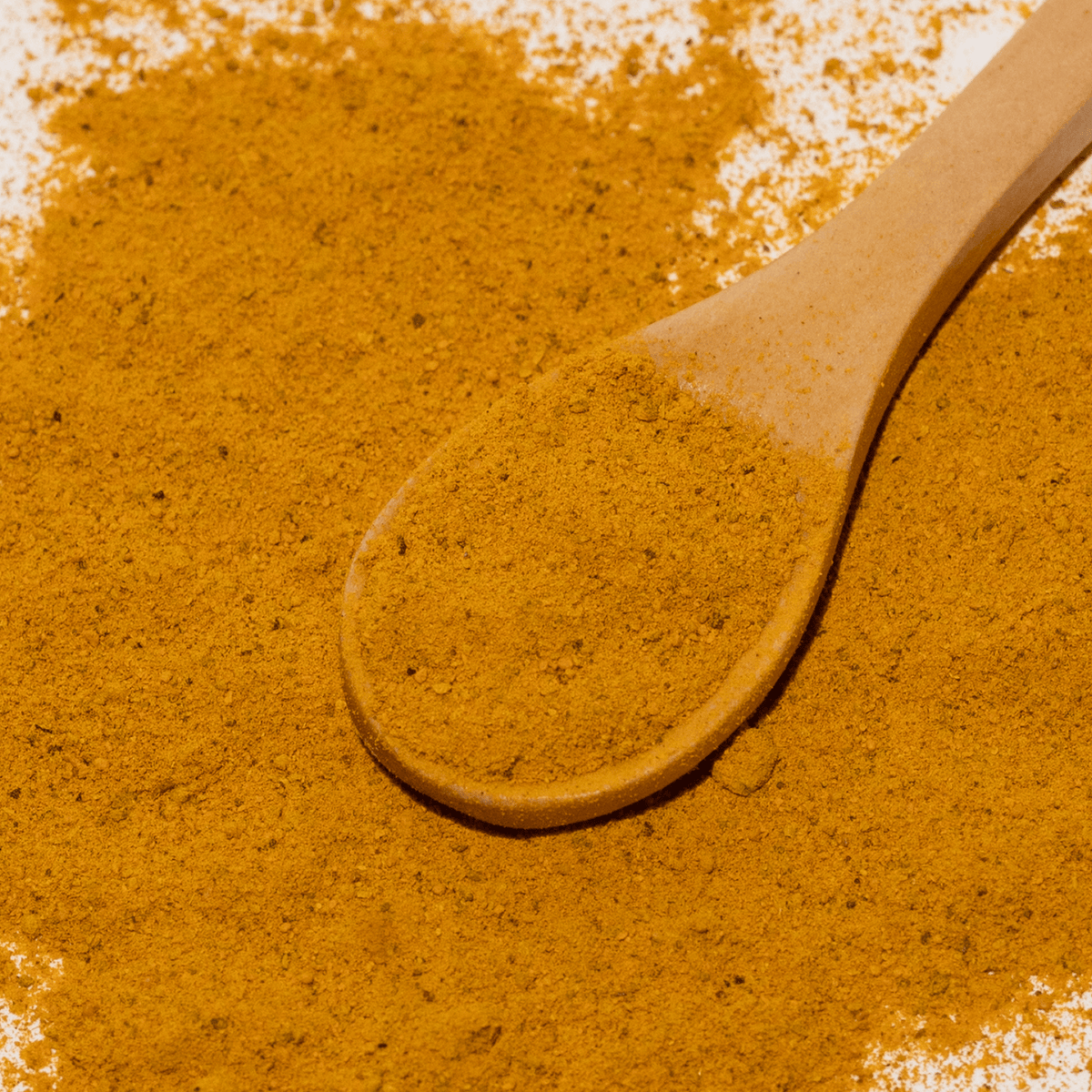 Wooden spoon with turmeric powder on a textured brown surface