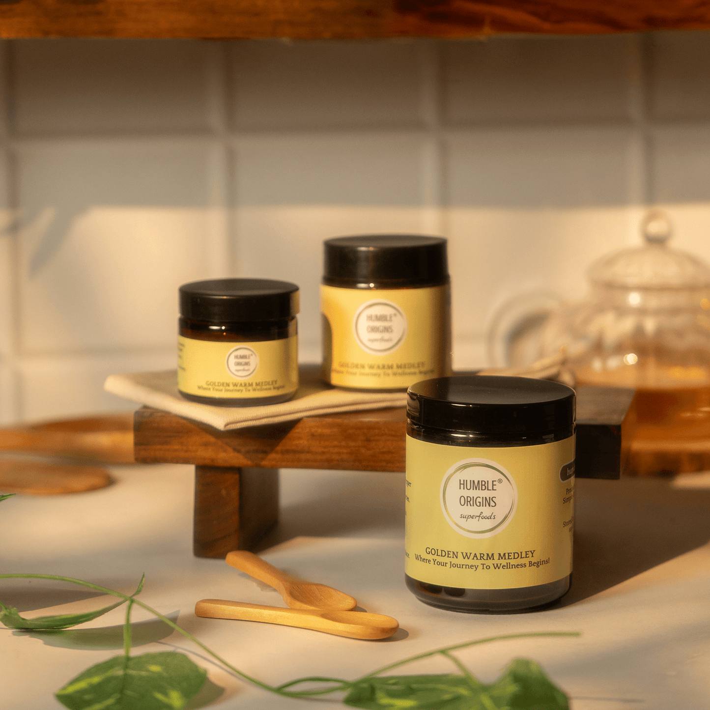 Jars of 'Humble Origins' Golden Warm Medley on a wooden shelf with a plant in the foreground.