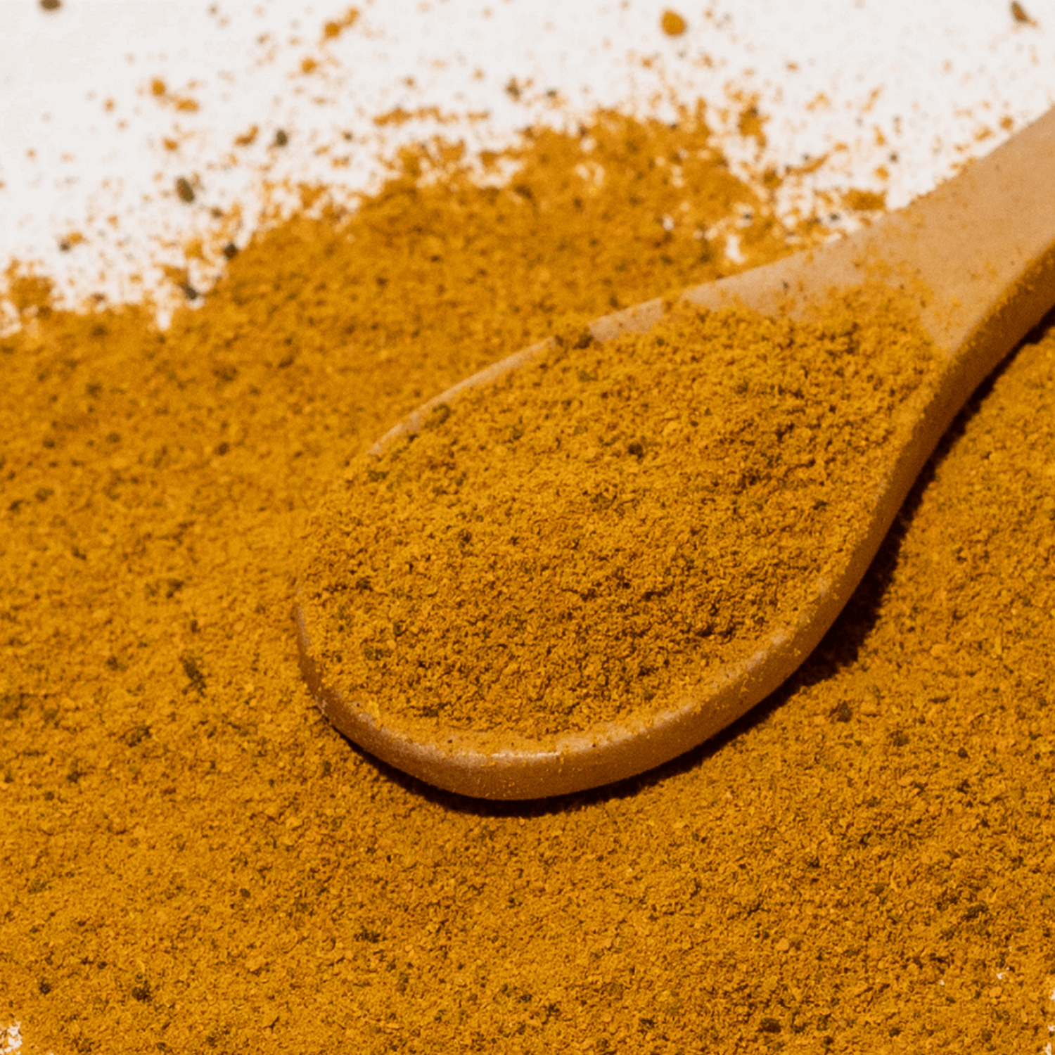 Wooden spoon filled with ground spice on a pile of the same spice.
