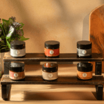 Set of jars on a wooden shelf with a plant in the background