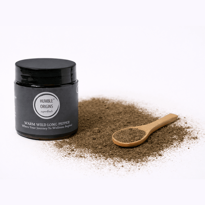 Black jar of 'Humble Origins' warm wild long pepper with a wooden spoon on a white background
