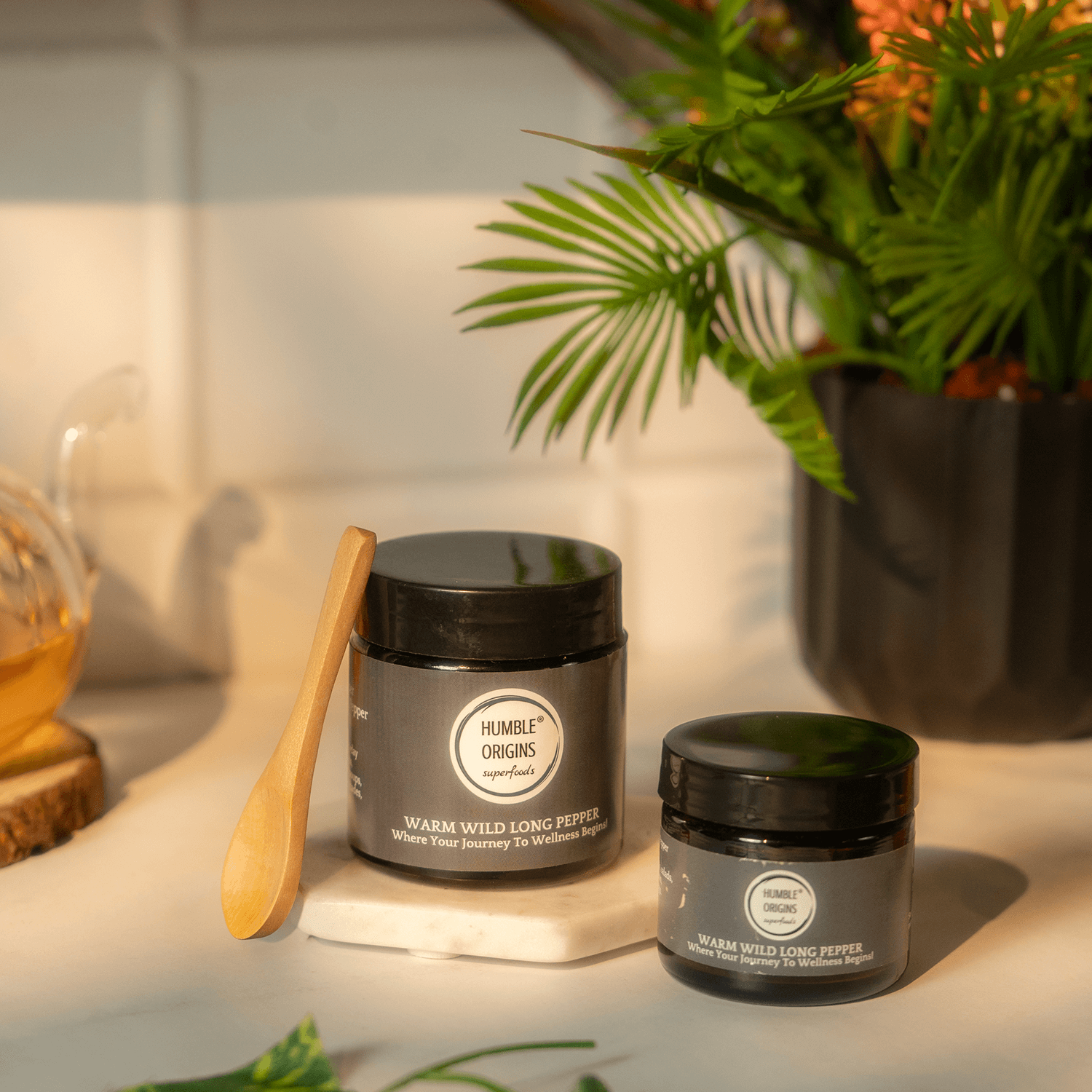 Two jars of long pepper product on a surface with a plant in the background