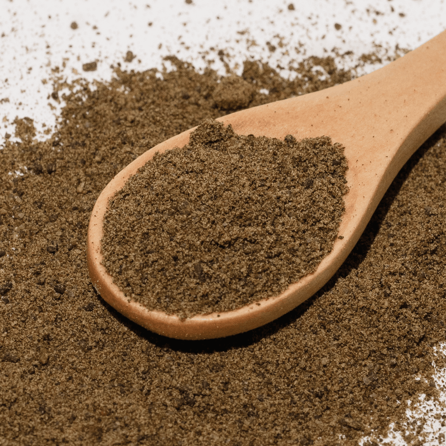 Wooden spoon filled with dark brown powder on a textured surface