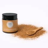 Jar of 'Humble Origins' natural product with a wooden spoon filled with powder on a white background